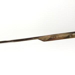 May include: Close-up of the arm of a pair of gold-tone glasses with the text "LUTHER 21657894" engraved on the metal.