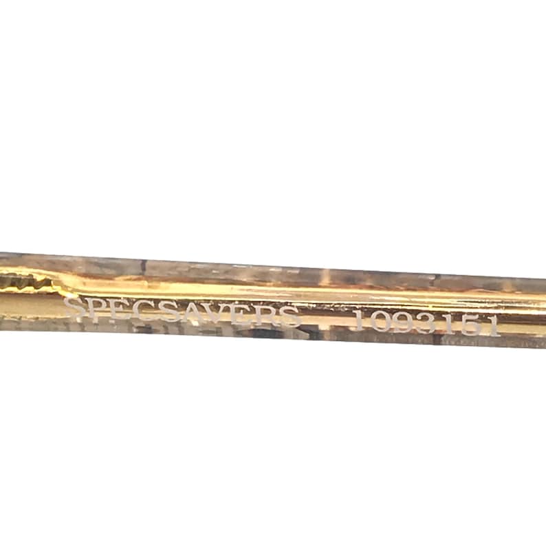 May include: Close-up of the gold-colored arm of a pair of glasses with the text "SPECSAVERS 1093151" printed on the arm.