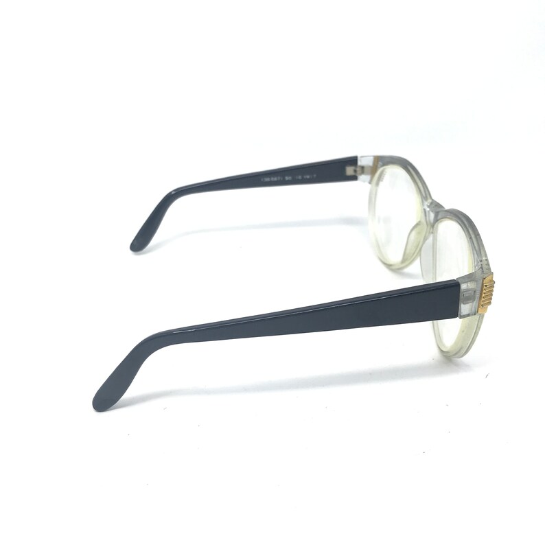 May include: Clear plastic framed glasses with black arms. The glasses have a gold accent on the side.