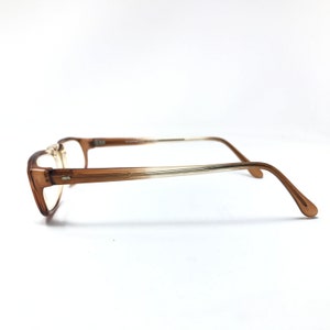 May include: Brown and gold-toned eyeglasses with a clear lens. The frame is made of plastic and has a gradient color.