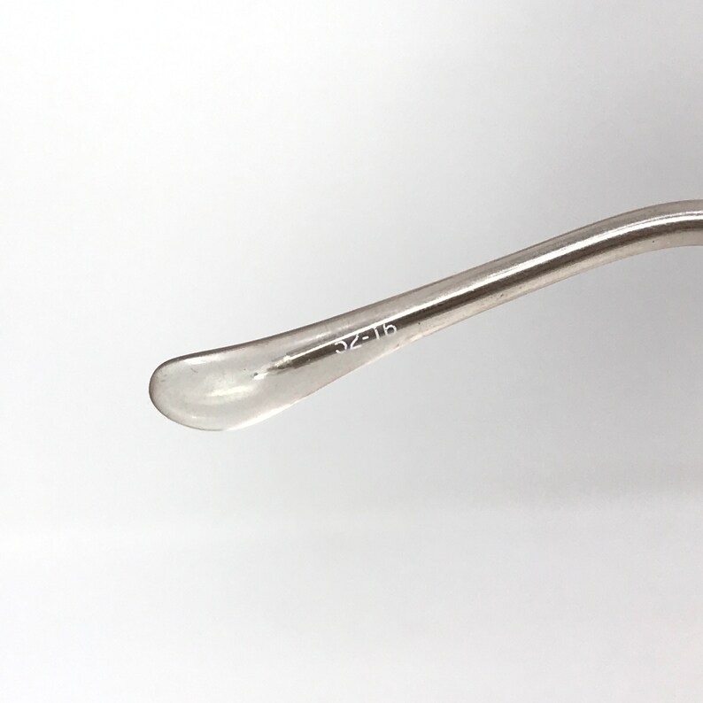 May include: Close-up of a clear eyeglass temple arm with the text "52-16" printed on the arm. The arm is curved and has a clear, rounded tip. The background is white.
