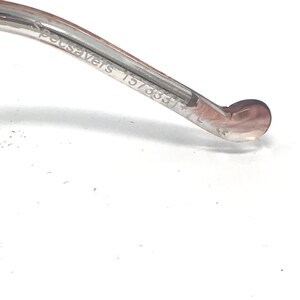 May include: Close-up of the arm of a pair of spectacles. The arm is clear with a brown tint and features the text "Specsavers 157333" and the letter "L". The end of the arm has a rounded shape.