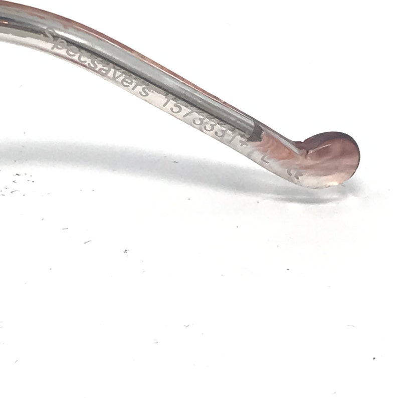 May include: Close-up of the arm of a pair of spectacles. The arm is clear with a brown tint and features the text "Specsavers 157333" and the letter "L". The end of the arm has a rounded shape.