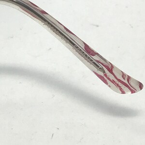 May include: Close-up of the arm of a pair of eyeglasses. The arm is clear with a pink and white zebra stripe pattern. The text "Persol" and other numbers are printed on the arm.