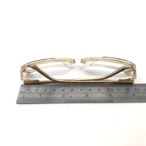 May include: A pair of gold-rimmed glasses with a brown tortoise shell pattern on the frame. The glasses are measured with a ruler, showing a length of 10 centimeters.