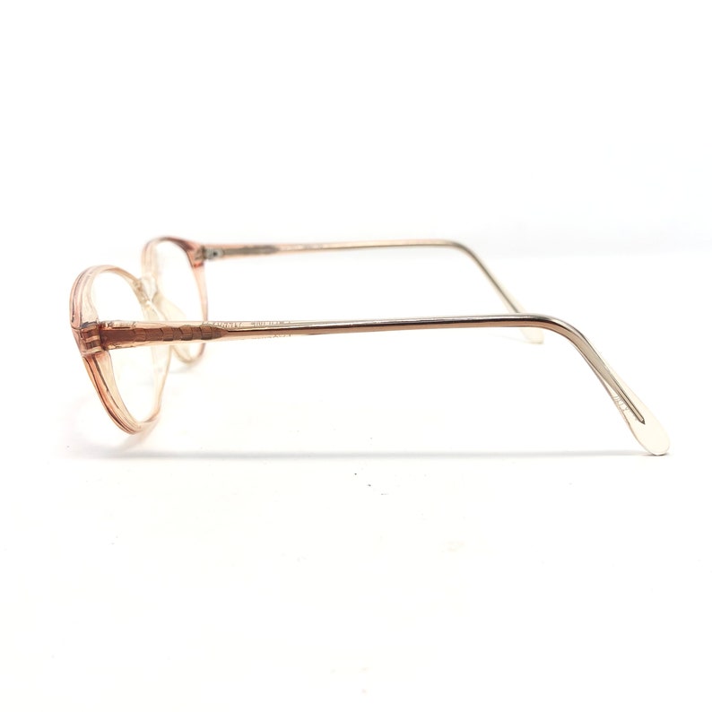 May include: Vintage eyeglasses with a light brown, oval frame and clear lenses. The temples are a light gold colour. The glasses are set against a white background.