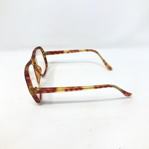 May include: A pair of vintage eyeglasses with a tortoiseshell pattern. The frames are a mix of brown and yellow, with a hexagonal shape. The temples are thin and extend to the ear pieces. The lenses are clear.