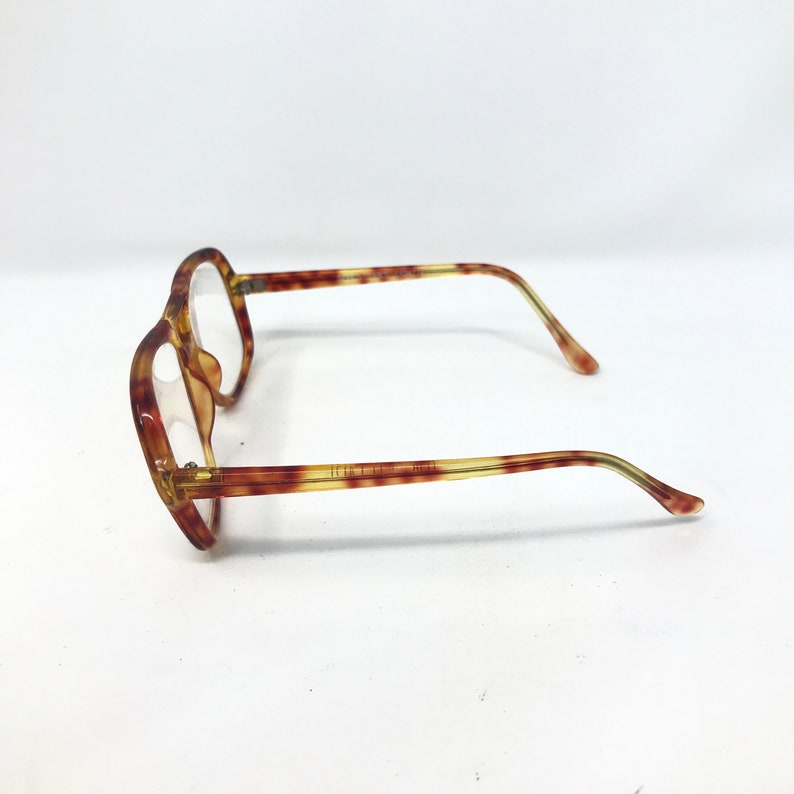 May include: A pair of vintage eyeglasses with a tortoiseshell pattern. The frames are a mix of brown and yellow, with a hexagonal shape. The temples are thin and extend to the ear pieces. The lenses are clear.