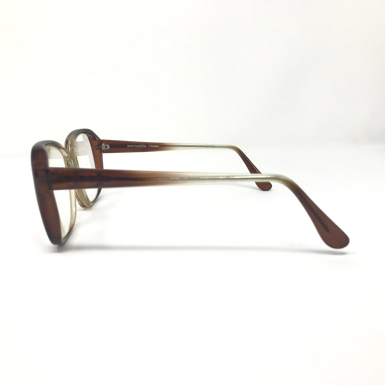 May include: Brown-framed eyeglasses with a classic design. The frames are a solid brown color, transitioning to a lighter shade towards the temples. The lenses are clear. The text "SPECSAVERS 1794294" is printed on the temple.