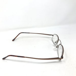 May include: A pair of eyeglasses with a rectangular frame and clear lenses. The frames are a dark brown color with a thin, wire-like design. The earpieces have a tortoiseshell pattern.