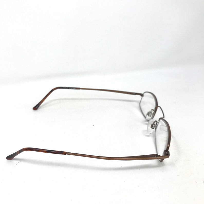 May include: A pair of eyeglasses with a rectangular frame and clear lenses. The frames are a dark brown color with a thin, wire-like design. The earpieces have a tortoiseshell pattern.