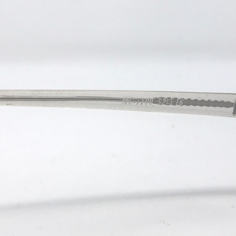 May include: Close-up of a clear eyeglass frame arm with the text "MC-1190 52 16" printed on it. The frame is made of a transparent material and is set against a white background.
