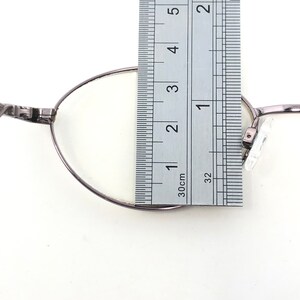 Peut inclure: Gros plan d'une paire de lunettes avec une r&egrave;gle. Les lunettes ont une monture m&eacute;tallique fine et des verres transparents. La r&egrave;gle indique les mesures en centim&egrave;tres, indiquant la taille des lunettes.