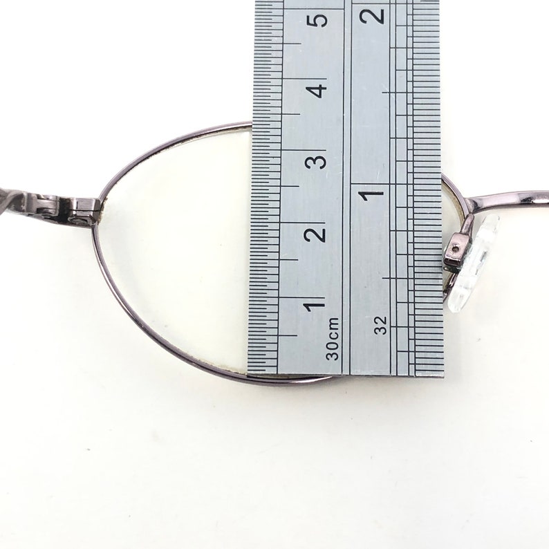 Peut inclure: Gros plan d'une paire de lunettes avec une r&egrave;gle. Les lunettes ont une monture m&eacute;tallique fine et des verres transparents. La r&egrave;gle indique les mesures en centim&egrave;tres, indiquant la taille des lunettes.