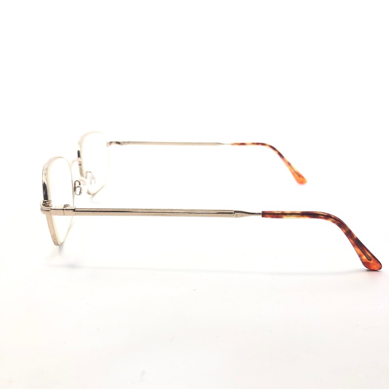 May include: Silver-coloured spectacles with a rectangular lens shape. The arms have a tortoiseshell pattern, and the glasses are set against a white background. The design is minimalist and classic.