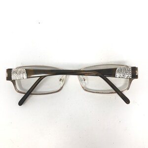 May include: Eyeglasses with a rectangular frame and clear lenses. The temples are dark brown with silver accents and rhinestones. The frame is a light brown color.
