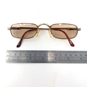 May include: Rectangular eyeglasses with brown tinted lenses and a gold-colored metal frame. The temples have a tortoiseshell pattern. The glasses are approximately 5.5 inches wide.
