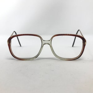 Op de afbeelding: Een bril met een helder, rechthoekig montuur en bruine accenten. De glazen zijn helder en de pootjes zijn dun en donker. De bril heeft een klassieke, vintage stijl.