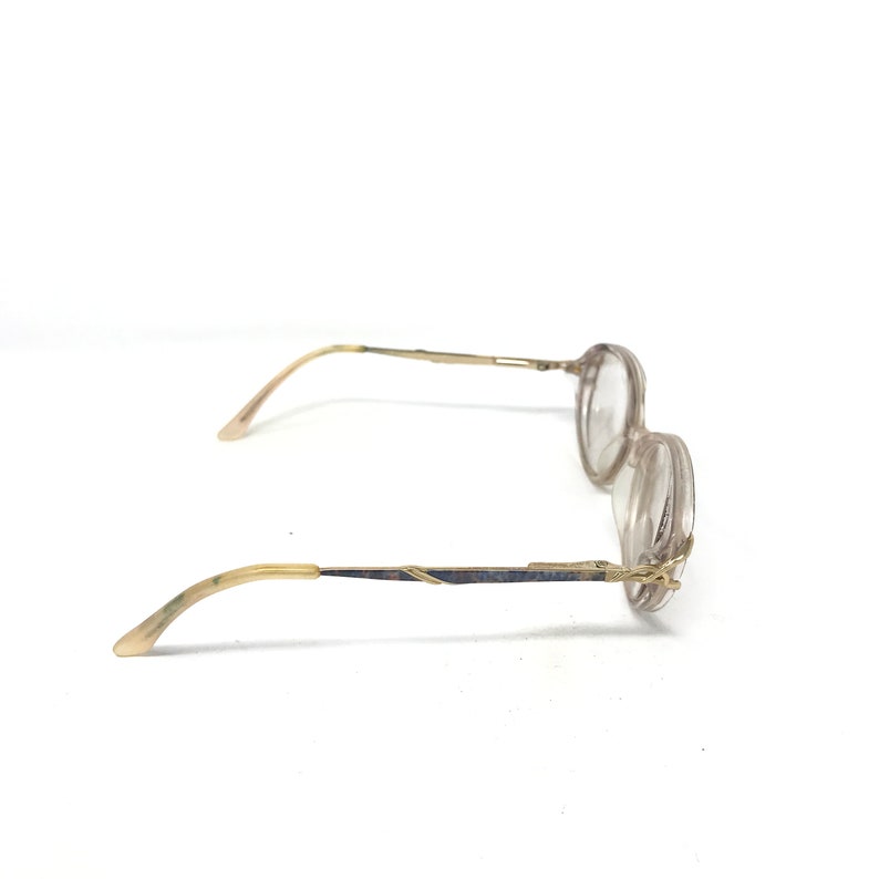 May include: A pair of vintage eyeglasses with a light brown frame and clear lenses. The temples are a light brown color with a gold-colored metal detail. The glasses are set against a white background.