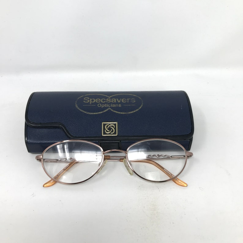 Op de afbeelding: Roze gouden bril met een blauwe etui met de tekst "Specsavers - Opticians".