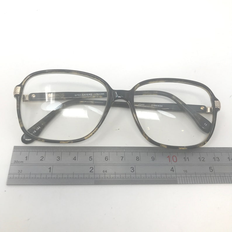 Puede incluir: Gafas con montura con estampado de carey. Las gafas tienen forma rectangular con bordes redondeados y lentes transparentes. El texto "SPECSAVERS-1764286" est&aacute; impreso en la montura. Una regla est&aacute; debajo.