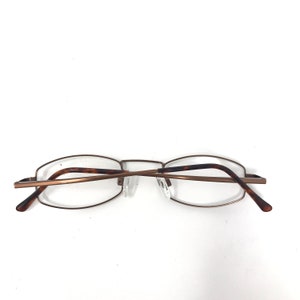 May include: A pair of eyeglasses with a thin, bronze-colored metal frame. The temples are a tortoiseshell pattern. The lenses are clear. The glasses are set against a white background.
