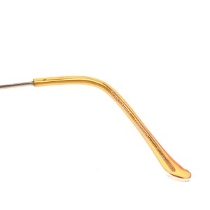Puede incluir: Primer plano de una patilla de gafas dorada. La patilla es curva y tiene el texto "Specsavers" y otro texto impreso. La patilla est&aacute; conectada a un alambre plateado.