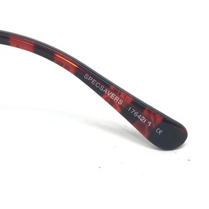 May include: Close-up of the arm of eyeglasses with a tortoiseshell pattern. The text "SPECSAVERS 17642 S CE" is printed on the arm. The arm is curved and has a glossy finish.