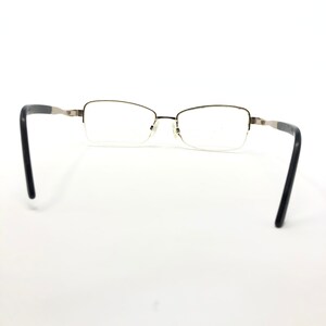 Pu&ograve; includere: Un paio di occhiali con design a mezza montatura. Le montature sono color oro metallizzato con aste nere. Le lenti sono trasparenti, su sfondo bianco.