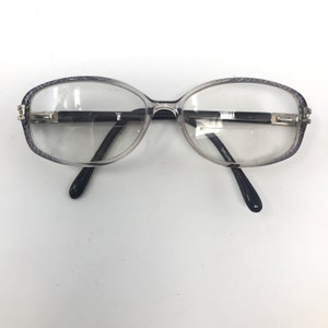 May include: Clear eyeglasses with oval lenses and a dark gray patterned frame. The temples are black, and the bridge is a dark color with silver accents. The glasses have the text "Spectre" on the temple.