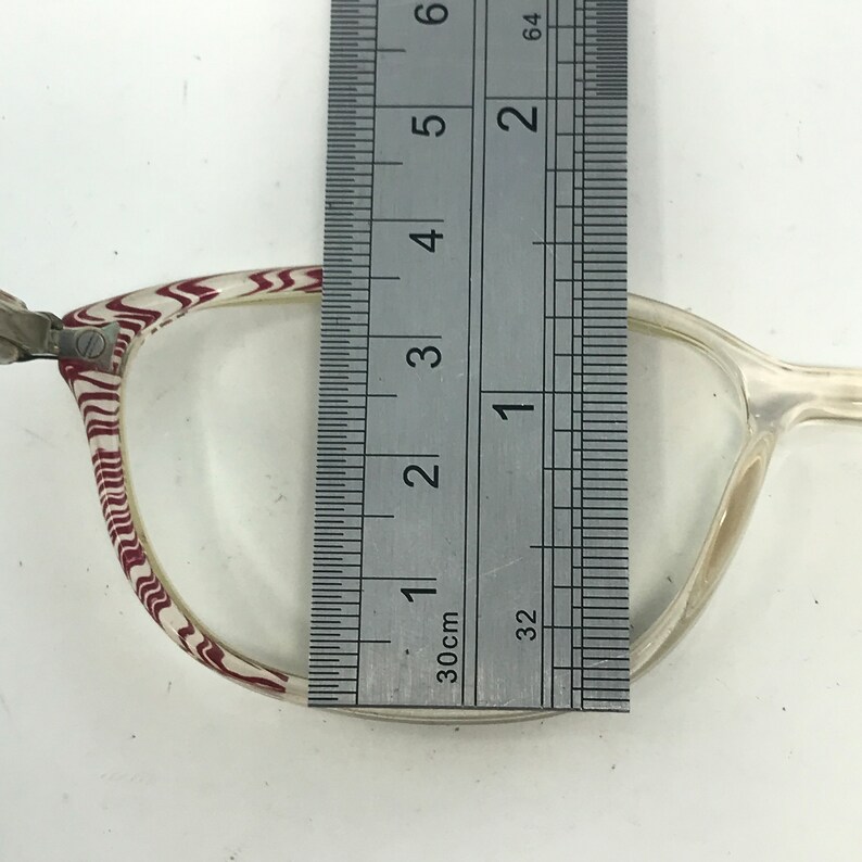 May include: Clear eyeglasses with a patterned frame in white and burgundy. A ruler is placed over the lens, measuring approximately 5 inches in height. The glasses have a classic, rectangular shape.