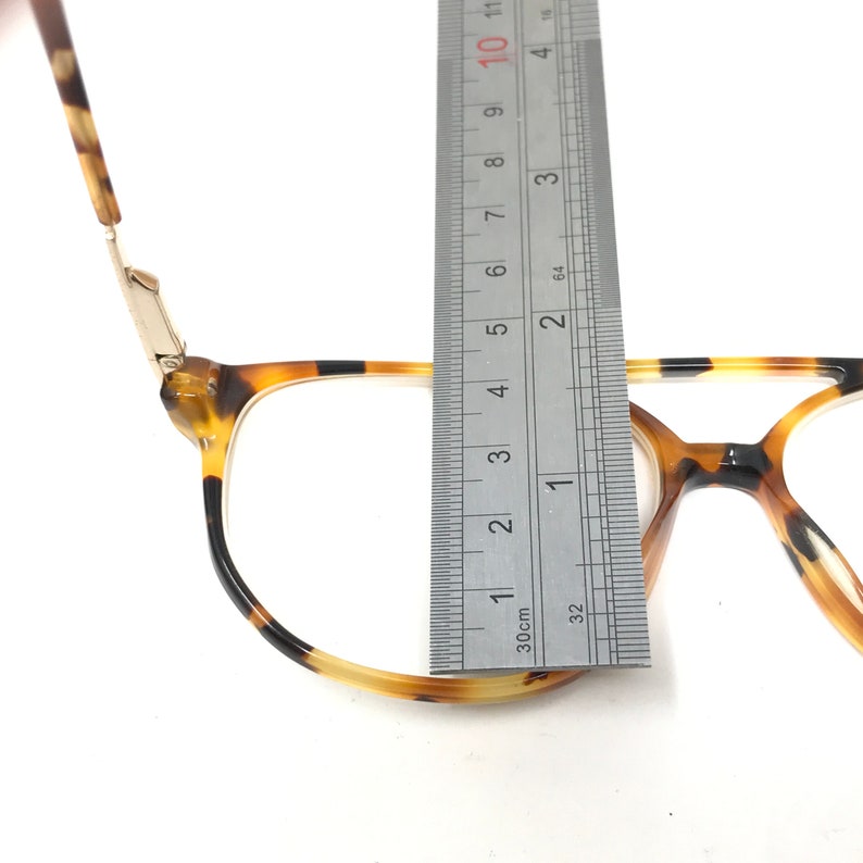 K&ouml;nnte beinhalten: Nahaufnahme einer Brille aus Schildpatt mit einem Metallgelenk. Die Brille wird mit einem Lineal gemessen, wobei die Breite des Rahmens 6,3 cm betr&auml;gt.