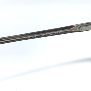 May include: Close-up of a silver-toned eyeglass frame. The text "PICTURE 52-18 COL 135" is etched on the temple arm. The frame is set against a white background.