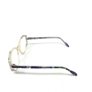 Puede incluir: Gafas transparentes con montura clara y patillas estampadas. Las lentes son redondas con una ligera forma hexagonal. Las patillas tienen un dise&ntilde;o moteado y colorido.