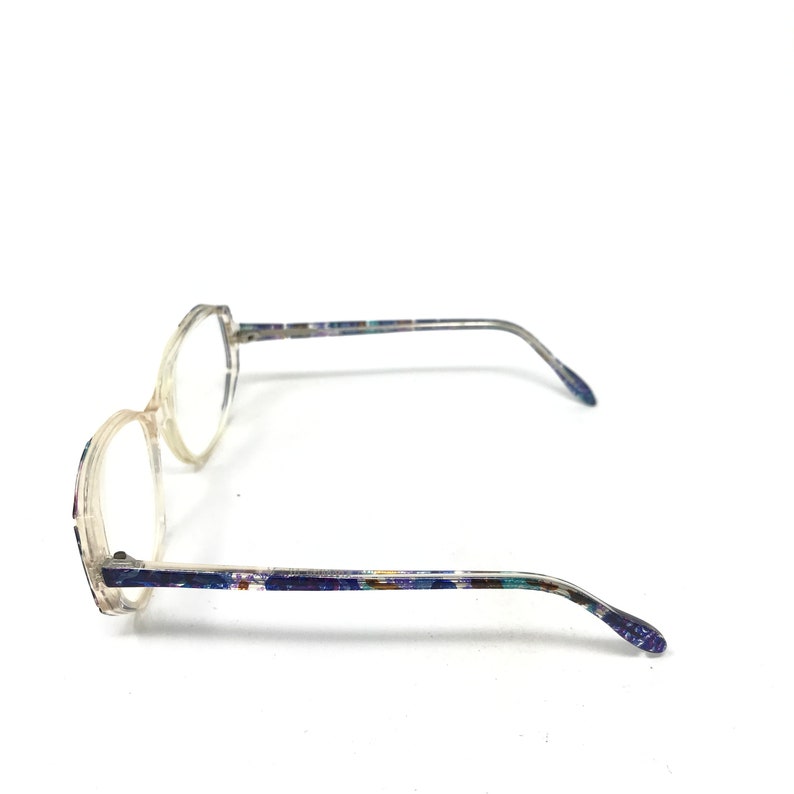 Puede incluir: Gafas transparentes con montura clara y patillas estampadas. Las lentes son redondas con una ligera forma hexagonal. Las patillas tienen un dise&ntilde;o moteado y colorido.