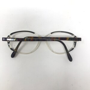May include: Eyeglasses with a clear frame and a patterned brown, green, and yellow top bar. The temples are dark brown and the lenses are clear. The glasses are set against a white background.