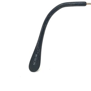 May include: Close-up of a black glasses arm with the measurements 54▢20-148 printed in white. The arm curves gently and has a textured surface. The background is white.