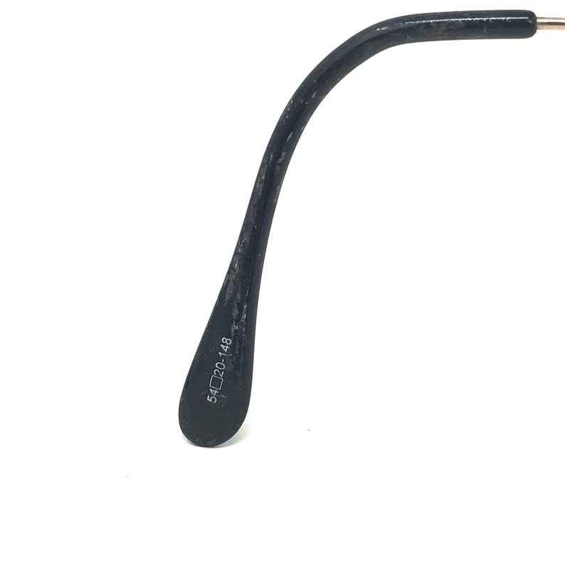 May include: Close-up of a black glasses arm with the measurements 54▢20-148 printed in white. The arm curves gently and has a textured surface. The background is white.