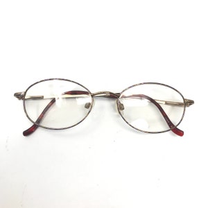 May include: Gold-rimmed oval eyeglasses with brown plastic arms.