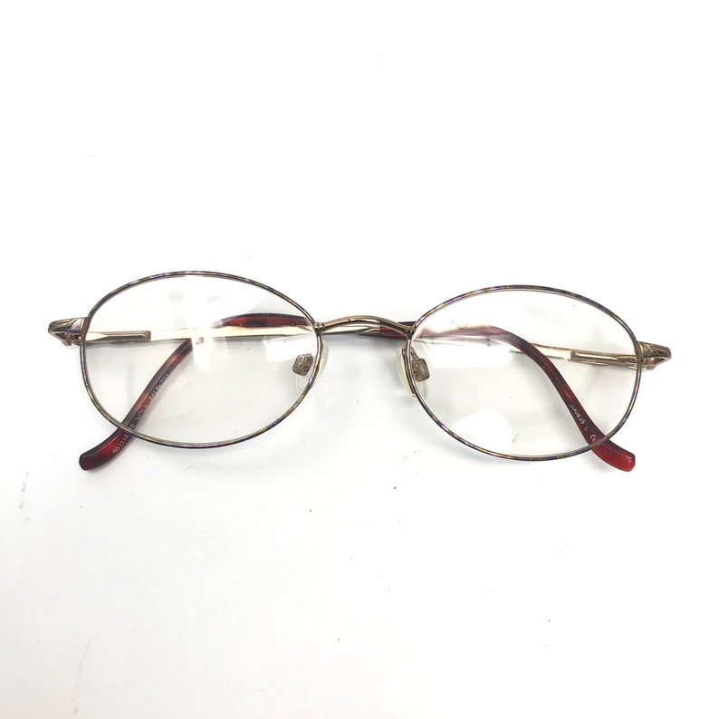 May include: Gold-rimmed oval eyeglasses with brown plastic arms.