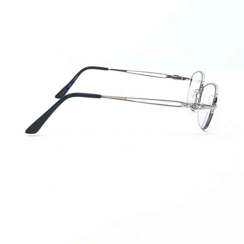 May include: Silver-toned eyeglasses with a thin frame and black temple arms. The glasses have a classic, minimalist design, suitable for everyday wear. The lenses are clear, and the overall aesthetic is modern and understated.