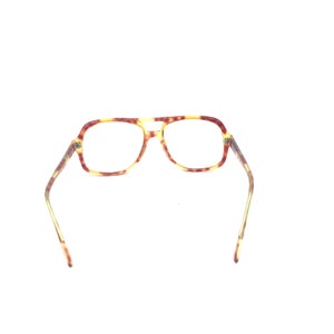 May include: A pair of eyeglasses with a tortoiseshell pattern. The frames have a rectangular shape with a double bridge and a light brown and yellow color scheme. The temples are thin and extend to the sides.