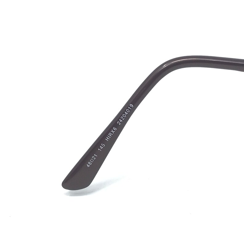 May include: Close-up of the temple arm of eyeglasses. The arm is dark brown and features the numbers "48021 145 HIRX6 24204019" printed in white. The glasses are set against a white background.