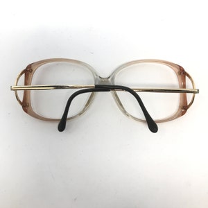 May include: Vintage eyeglasses with a clear and brown gradient frame, gold-tone metal accents, and black temples. The glasses have a rectangular shape and are designed for vision correction.