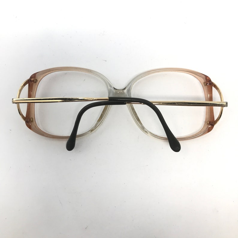 May include: Vintage eyeglasses with a clear and brown gradient frame, gold-tone metal accents, and black temples. The glasses have a rectangular shape and are designed for vision correction.