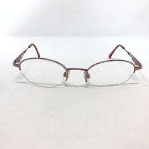 May include: A pair of oval-shaped eyeglasses with a bronze-colored metal frame. The lenses are clear, and the frame has a delicate, minimalist design. The temples feature a decorative, twisted pattern.