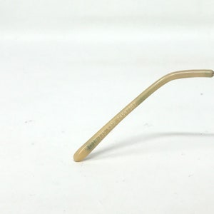 May include: A close-up of the arm of a pair of eyeglasses. The arm is a light beige color and has the text "50▢19-135 Kate 24547307" printed on it. The end of the arm is rounded.