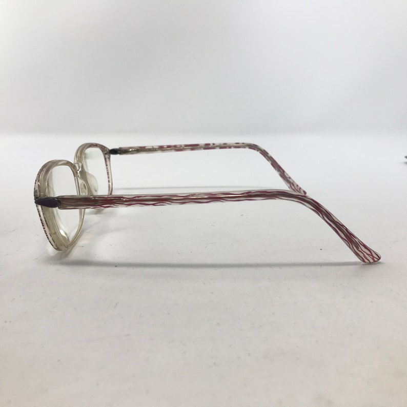 May include: Clear eyeglasses with a rectangular frame and red and white striped temples. The glasses have a classic design, suitable for everyday use. The lenses are clear, and the frame is made of a lightweight material.