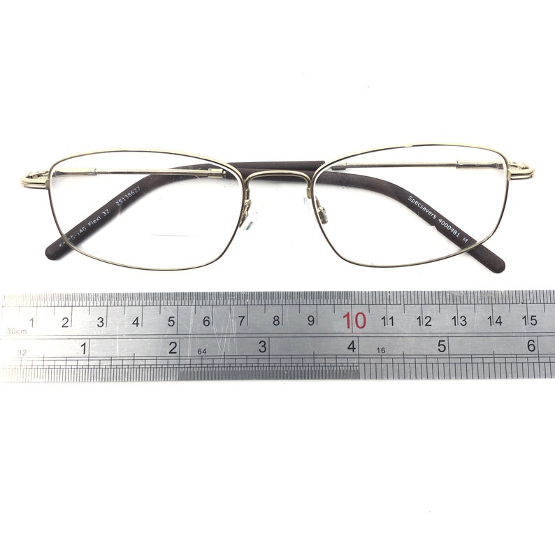 May include: Gold-rimmed eyeglasses with rectangular lenses and dark brown temples. The glasses are positioned above a ruler, with the frame measuring approximately 5.9 inches in width. The text on the frame reads "Specsavers 4000481 M".