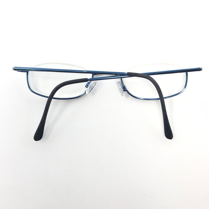 May include: Blue rimless eyeglasses with a thin, rectangular frame and black temple arms. The lenses are clear, and the glasses are set against a white background. The glasses are designed for vision correction.